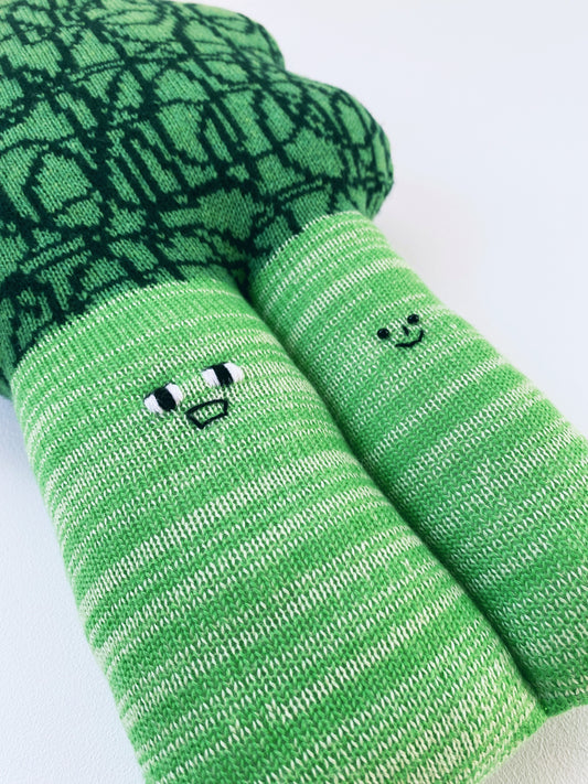 Soft knitted lambswool broccoli toy plush cushion with smiley face designs on a light gray background
