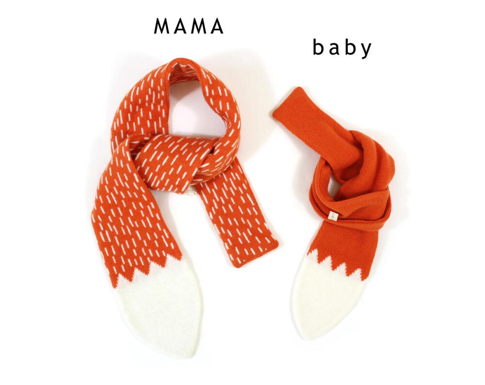 Two orange knitted lambswool scarves resembling a fox tail, one with a pattern and one plain, labeled 'MAMA' and 'baby' on a white background.