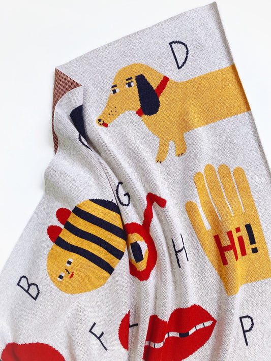 Alphabet knit blanket with cartoon dog, bee, and letters on a white background