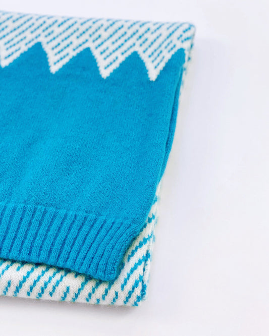 Folded blue and white knitted scarf with mountain design on a white background