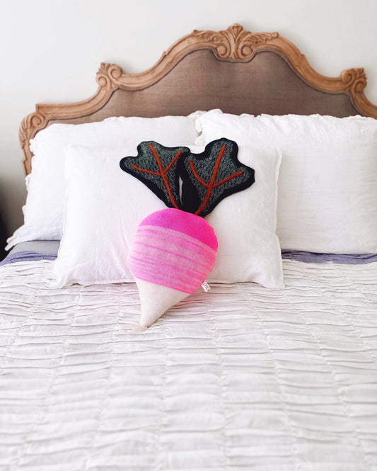 Decorative radish shaped pillow with a unique design on a bed with a wooden headboard.