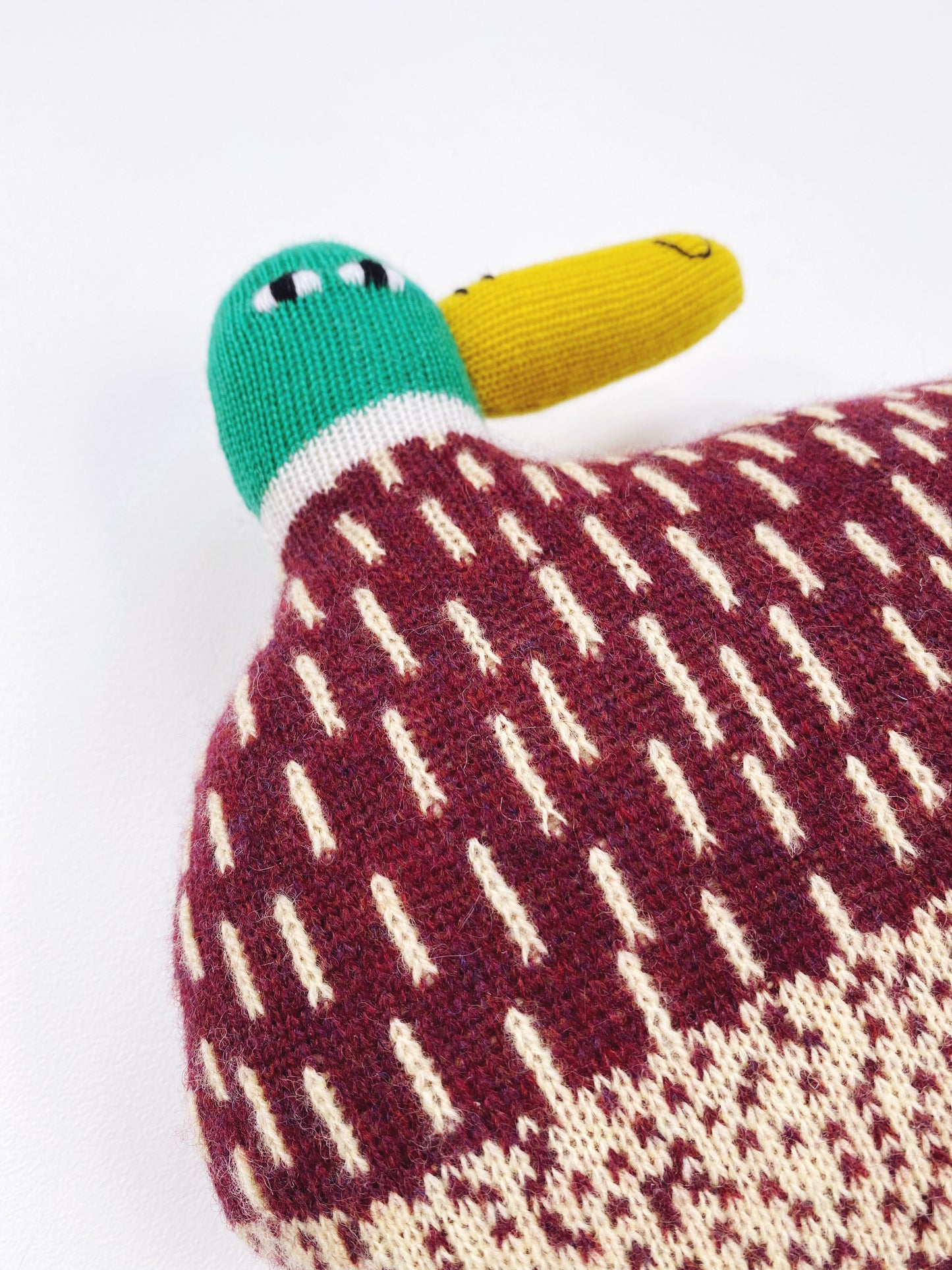 Knitted duck-shaped toy cushion with a patterned body on a white background