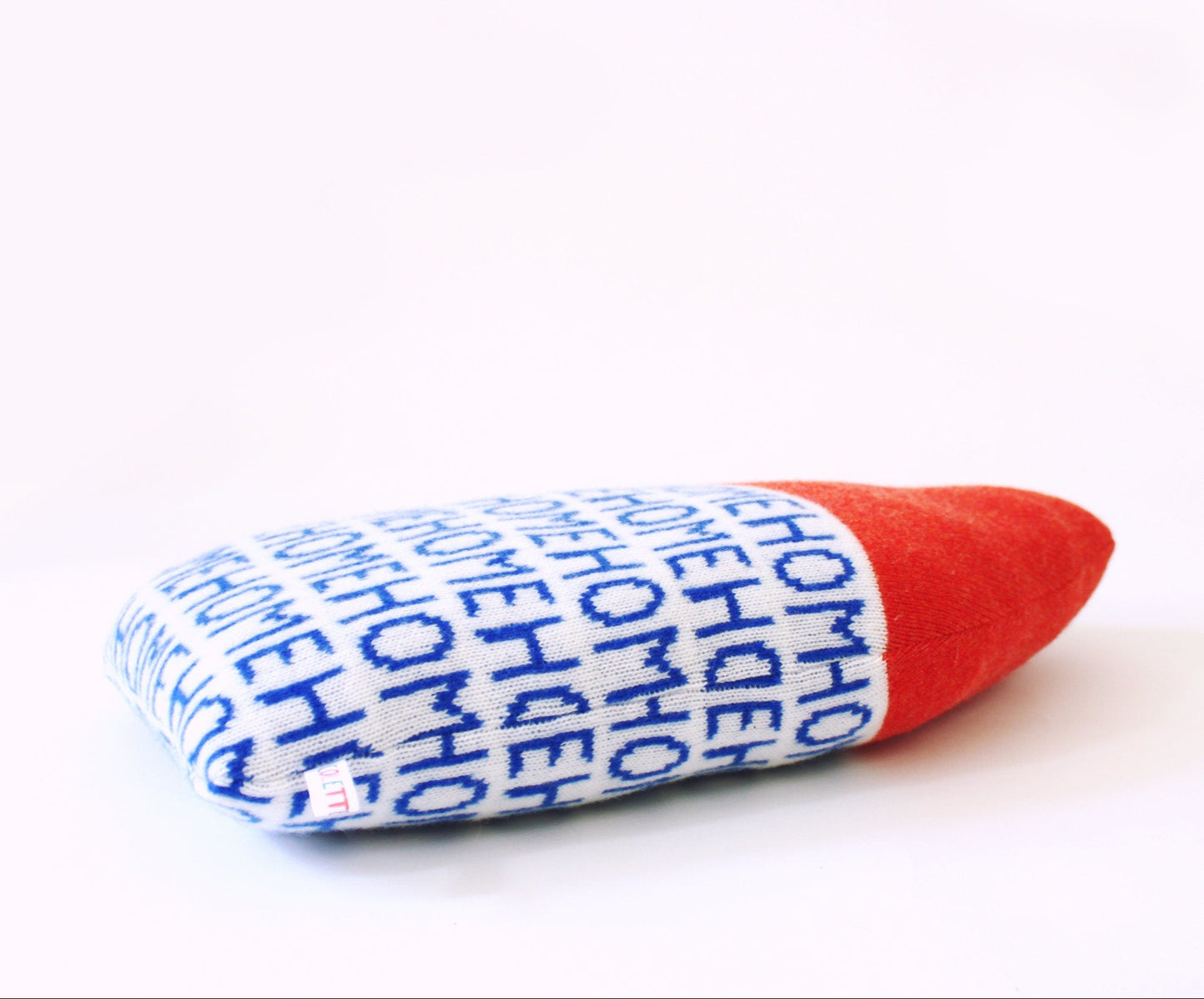 Textured pillow resembling a house with blue text and red roof on a white background