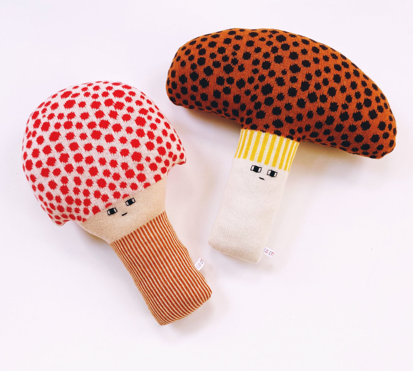 Two plush toys resembling mushrooms with faces on a white background