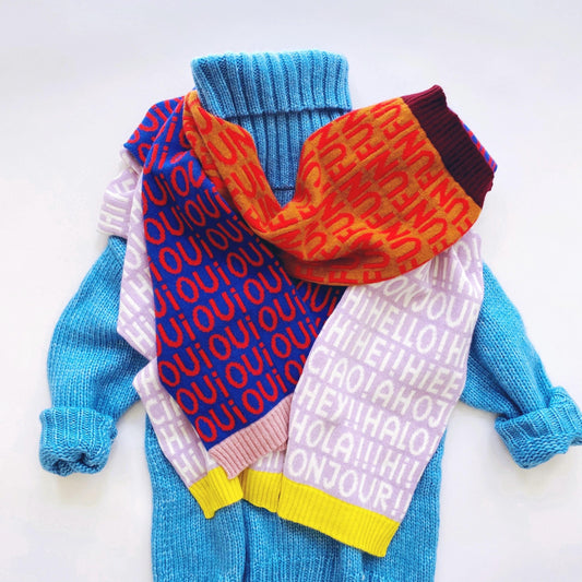 Colorful knitted scarves with text patterns draped over a blue sweater on a white background