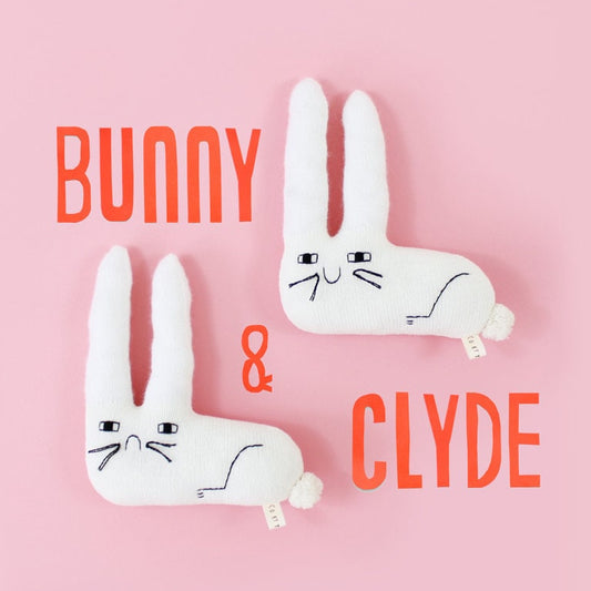 Two white rabbit knitted plush toys with 'Bunny' and 'Clyde' text on a pink background