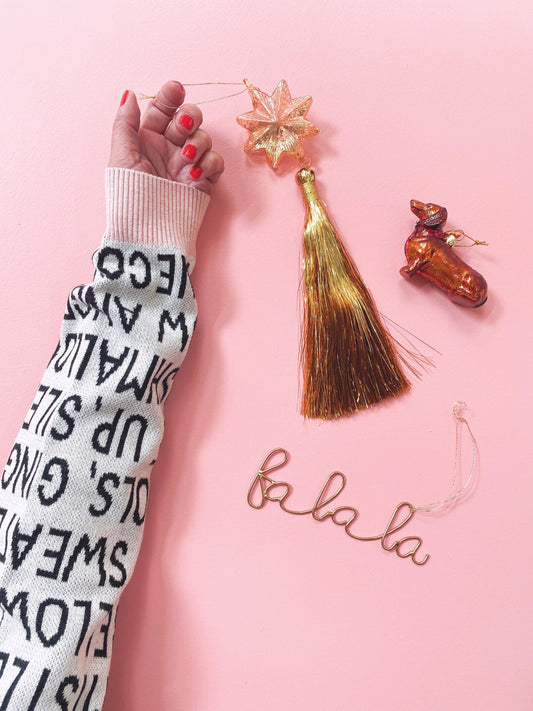 Hand wearing a patterned sweater with Christmas decorations on a pink background