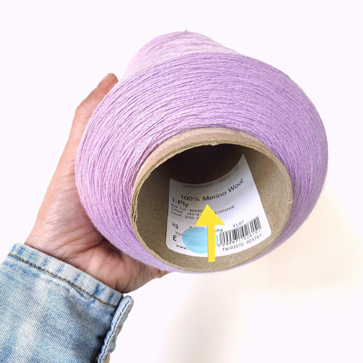 Hand holding a roll of purple yarn with a label on a white background