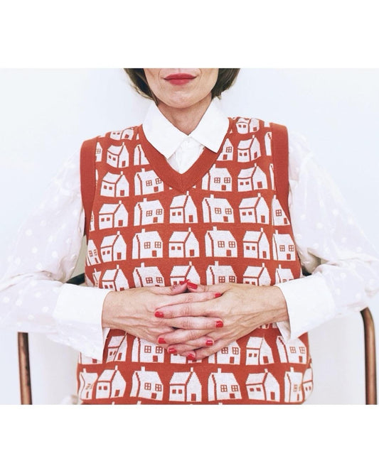 Person wearing a knit sweater vest with white house pattern on a white background