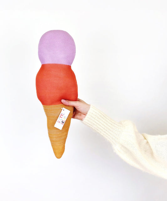 Hand holding a plush ice cream cone toy with a purple top, red middle, and yellow bottom on a white background.