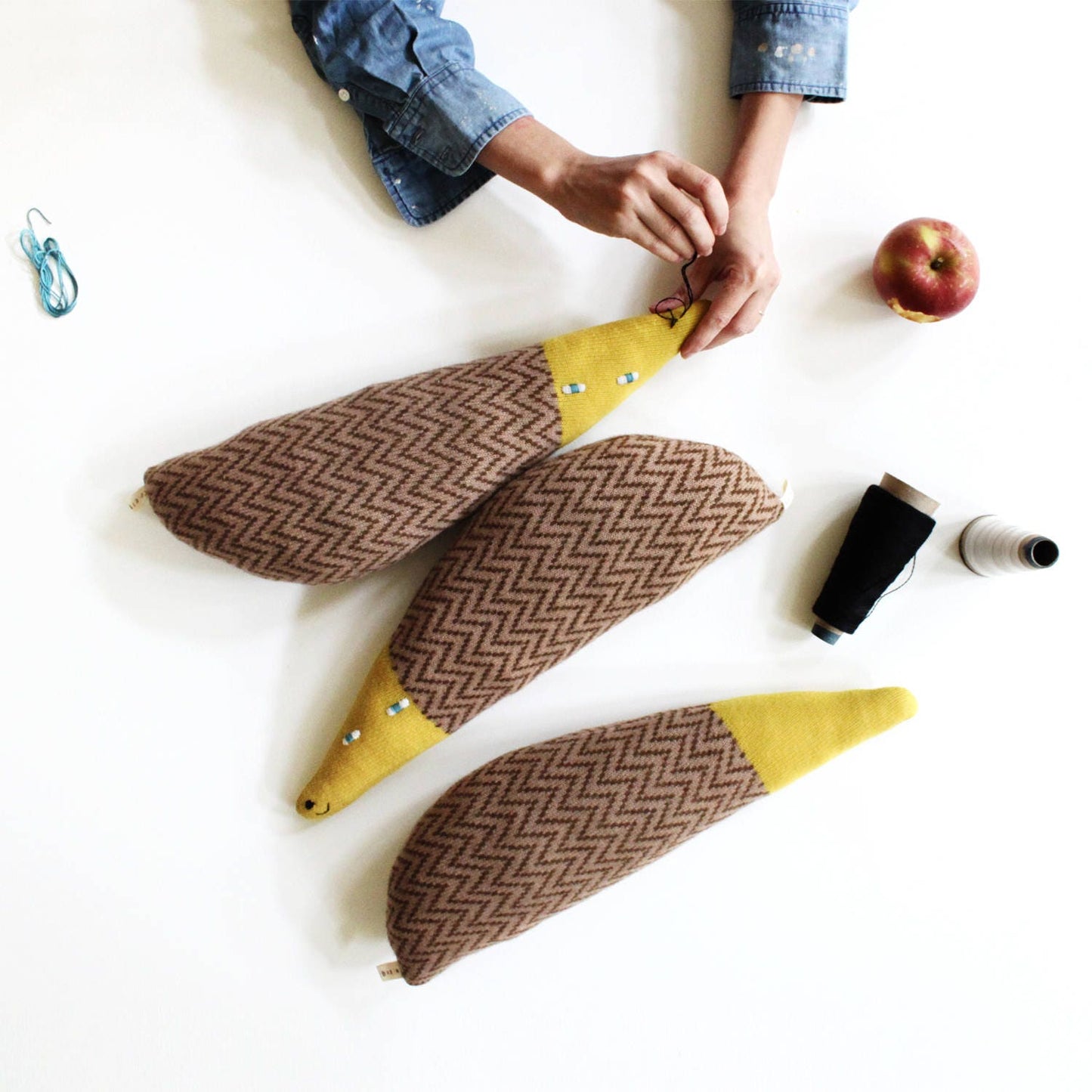 Person working on a craft project with fabric pieces and hedgehog shaped plush toys on a white surface