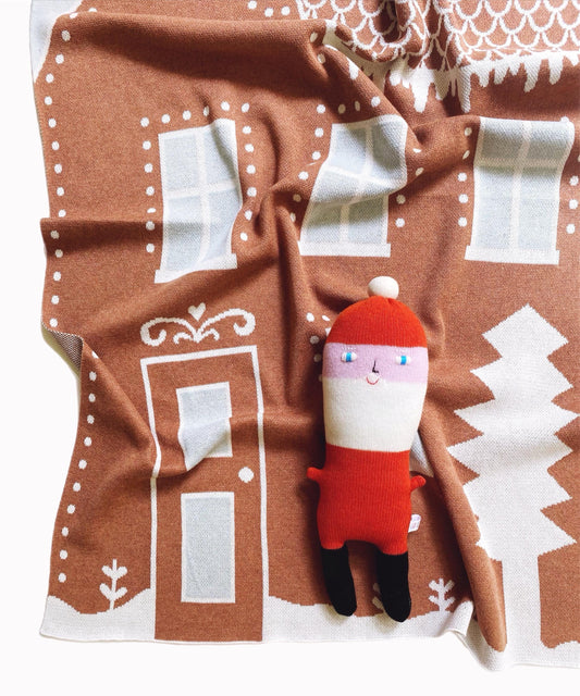 Santa Claus plush toyon a gingerbread house patterned knitted blanket