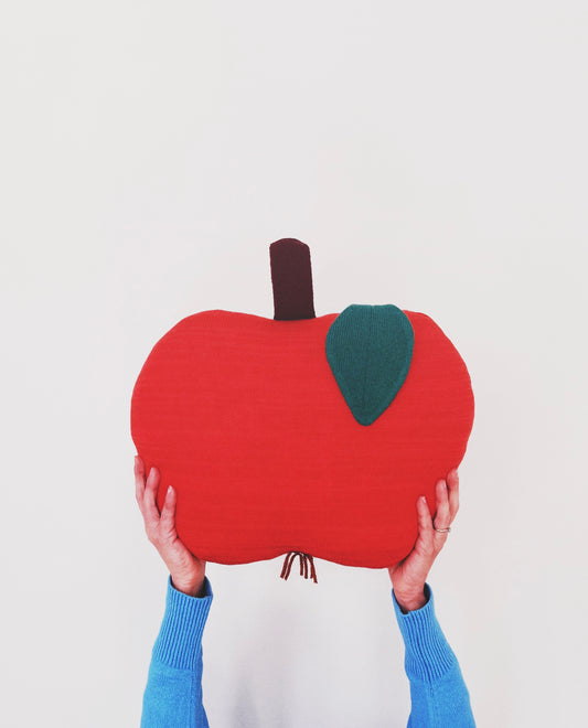 Person holding a red apple-shaped pillow against a white background