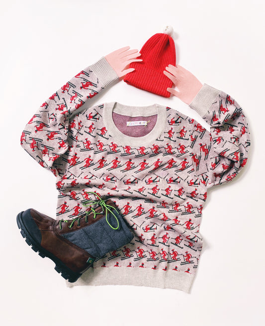 Knitted sweater with red and black pattern of skiers, red beanie, and brown boots on a white background