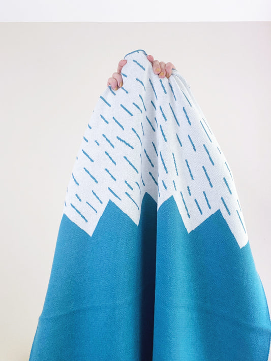 Blue and white mountain patterned knitted blanket held by a person against a plain background