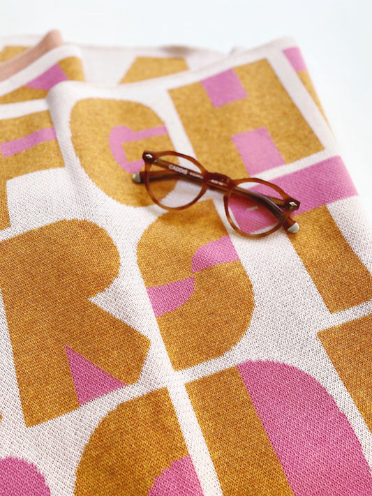 Glasses on a knit blanket surface with a pattern of large, colorful letters.