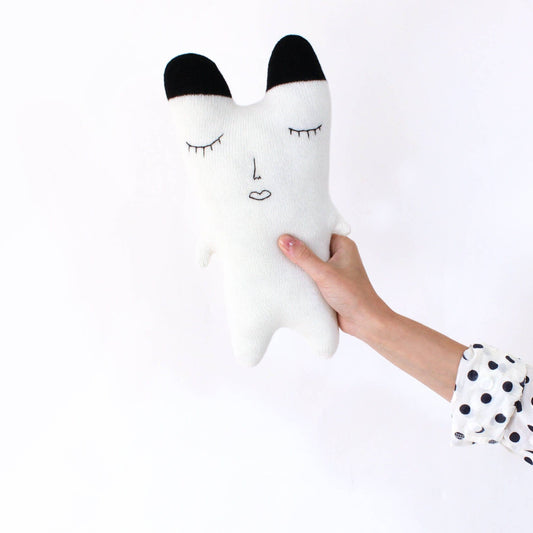White knitted polar bear plush toy with black accents held by a hand on a white background