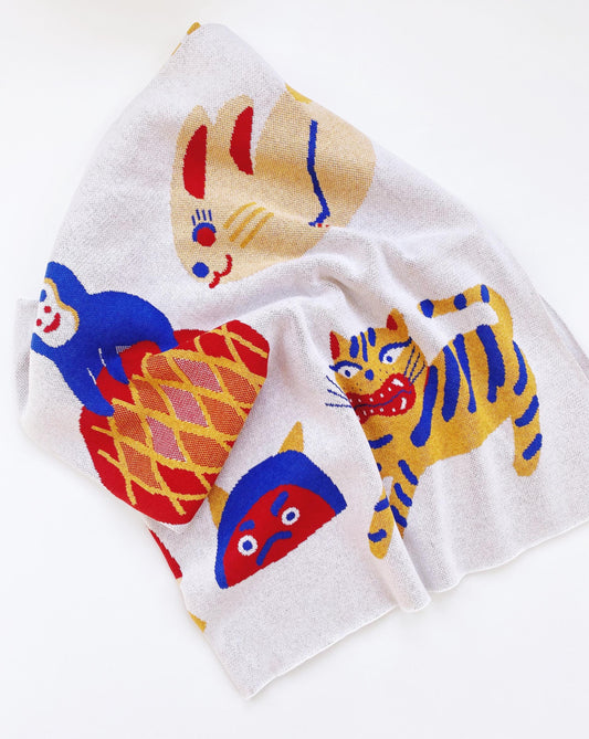 White knitted blanket with colorful tiger illustrations and other japanese characters on a white background