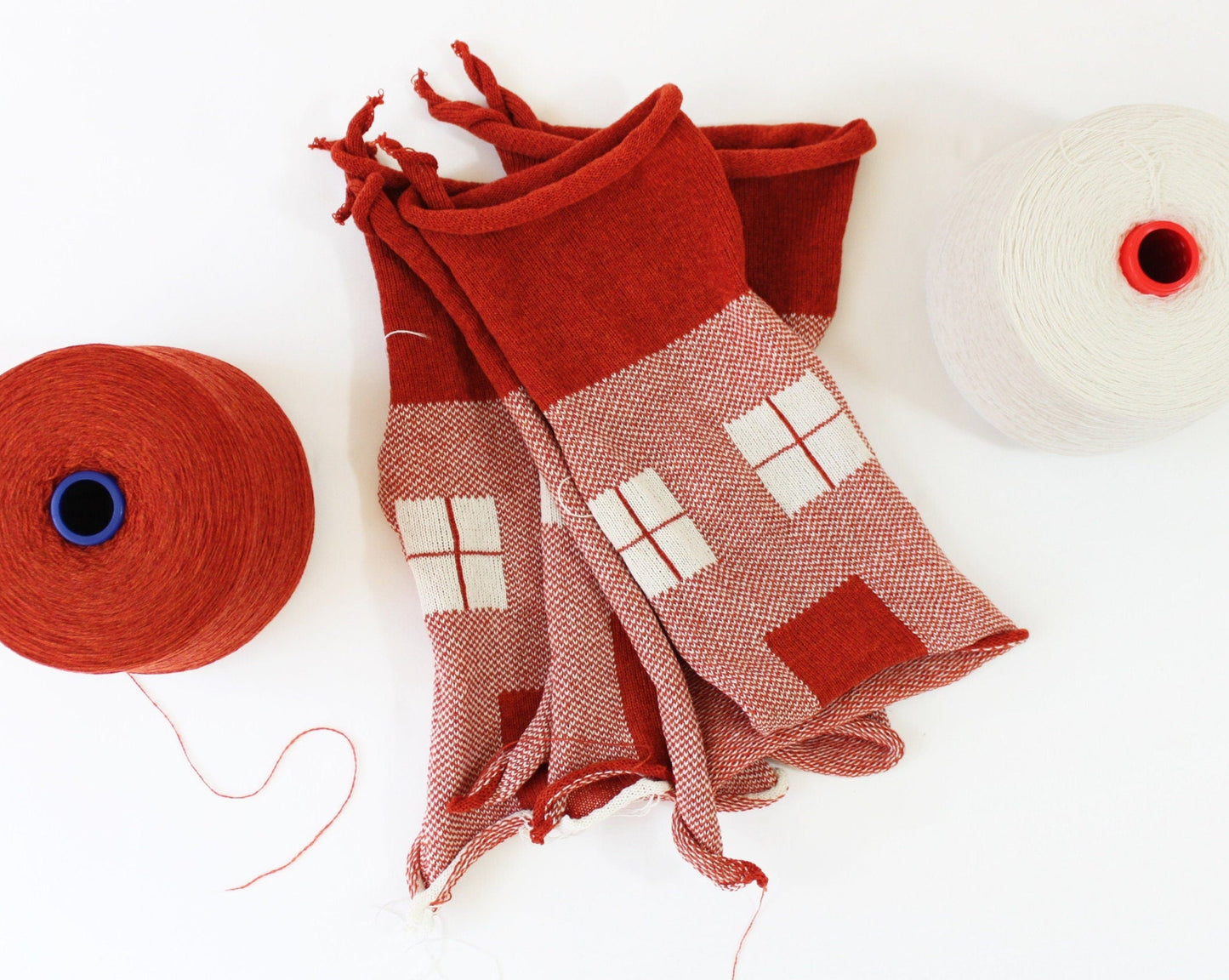 Red scarf with house pattern and two red yarn balls on a white background