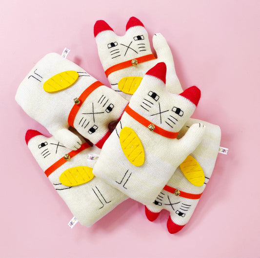 Set of white cat-shaped manekineko plush toys with red and yellow accents on a pink background