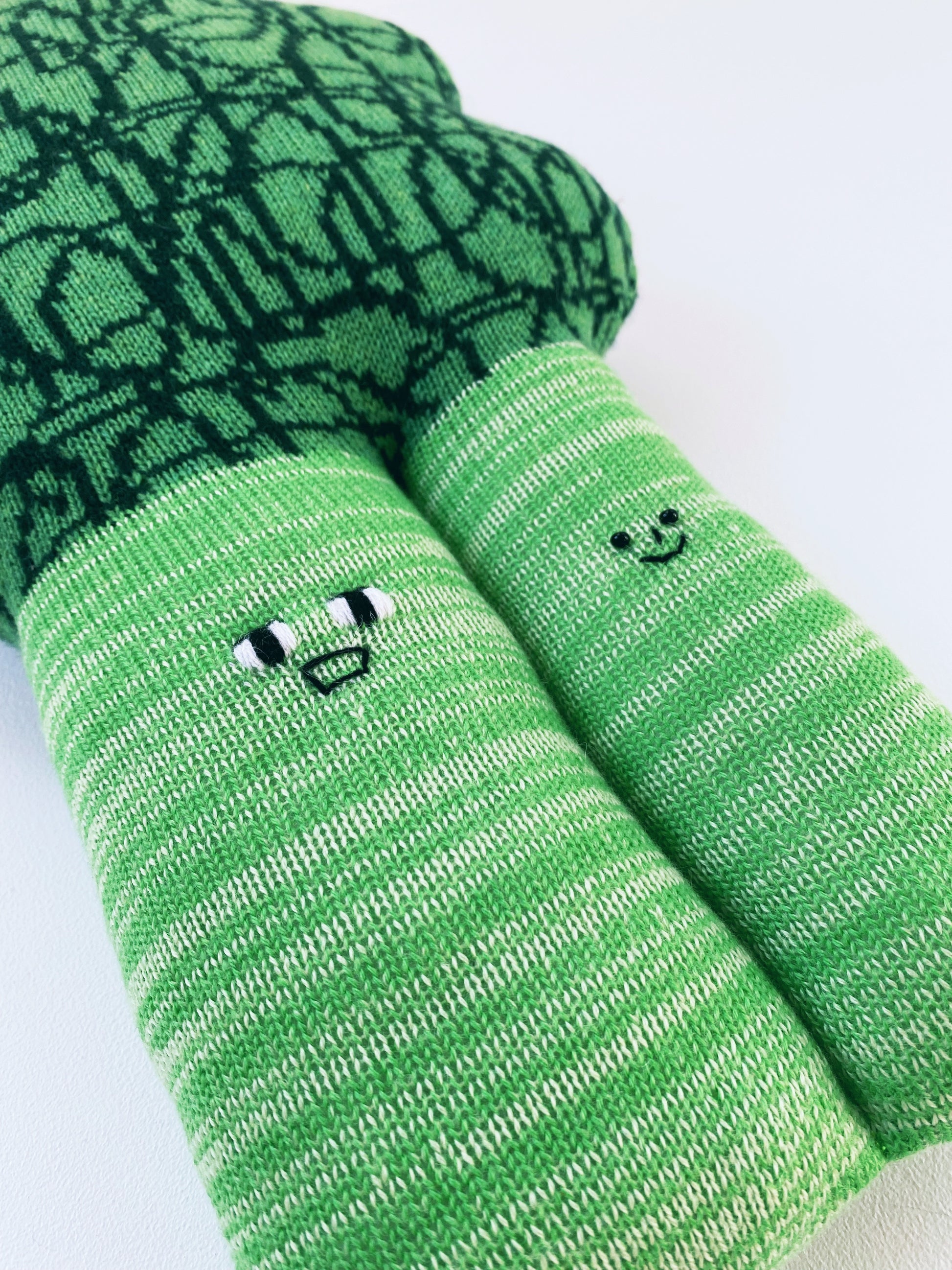 Soft knitted lambswool broccoli toy plush cushion with smiley face designs on a light gray background