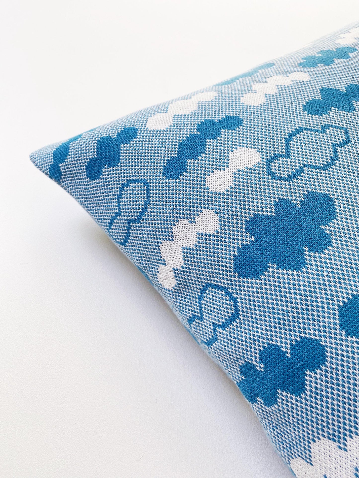 Detail of a knitted pillow with blue and white cloud pattern on a white background