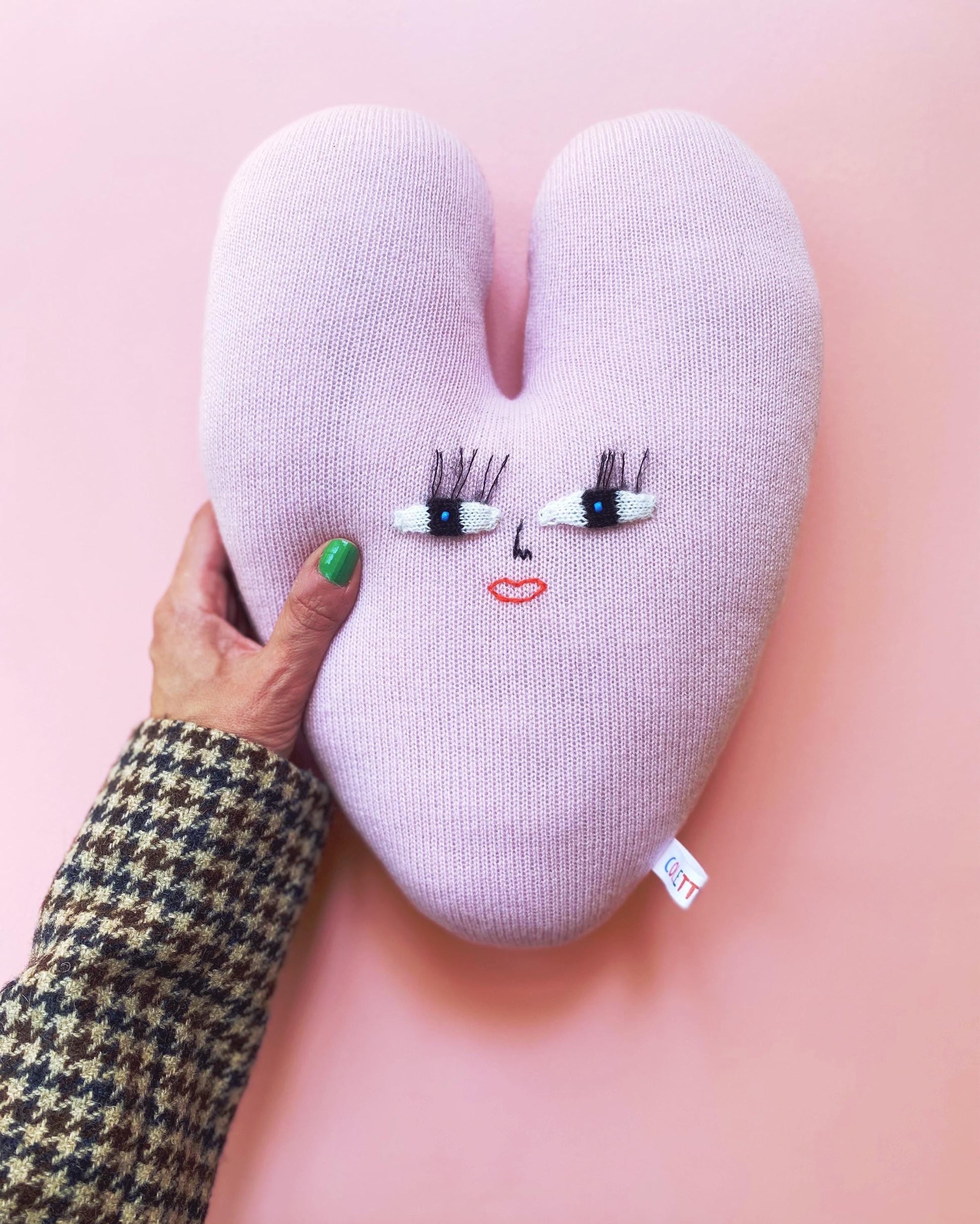 Heart-shaped knitted cushion with face embroidery on a pink background