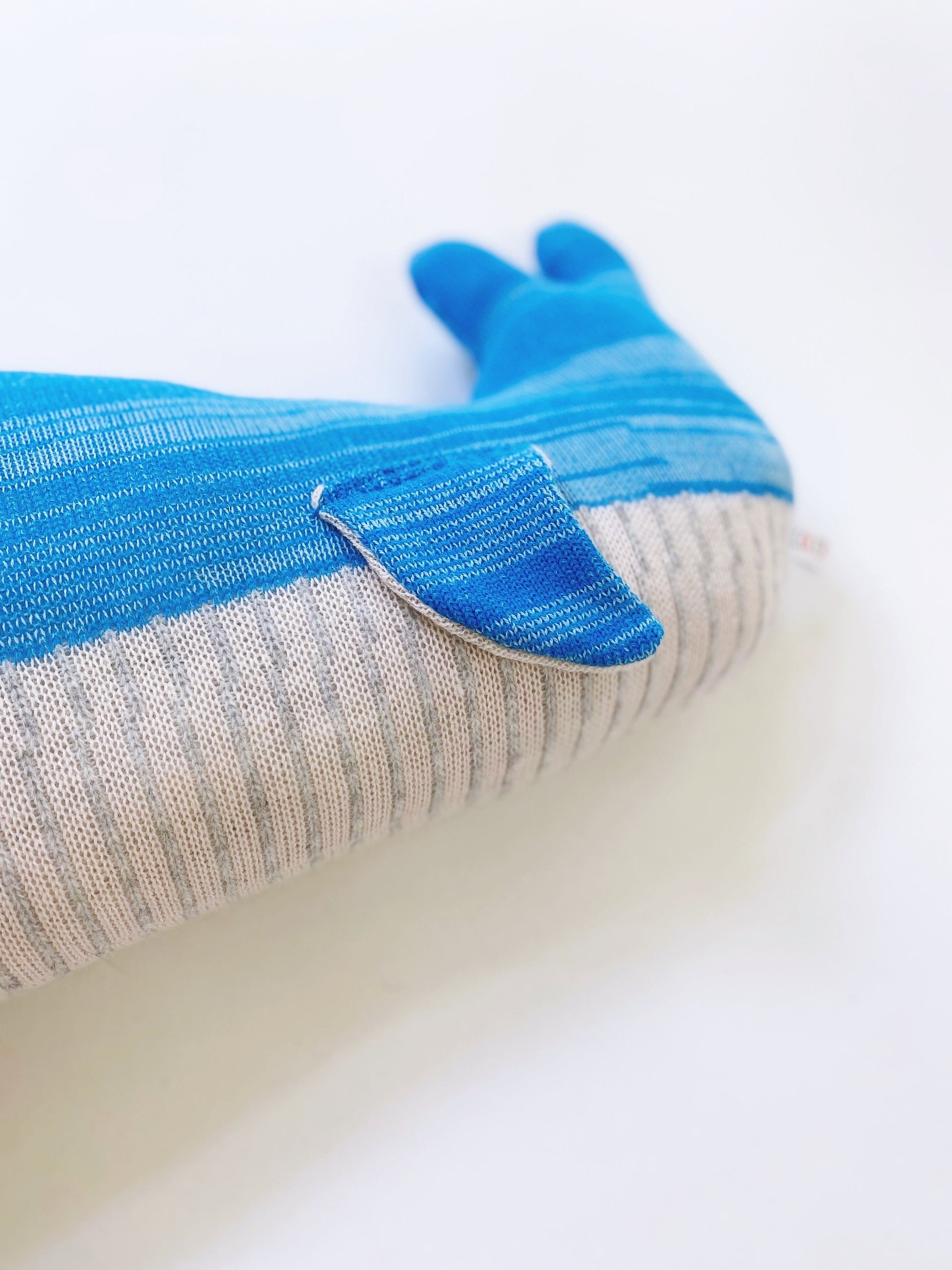 Close-up of a soft knitted whale toy pillow plush with blue and gray pattern on a white background