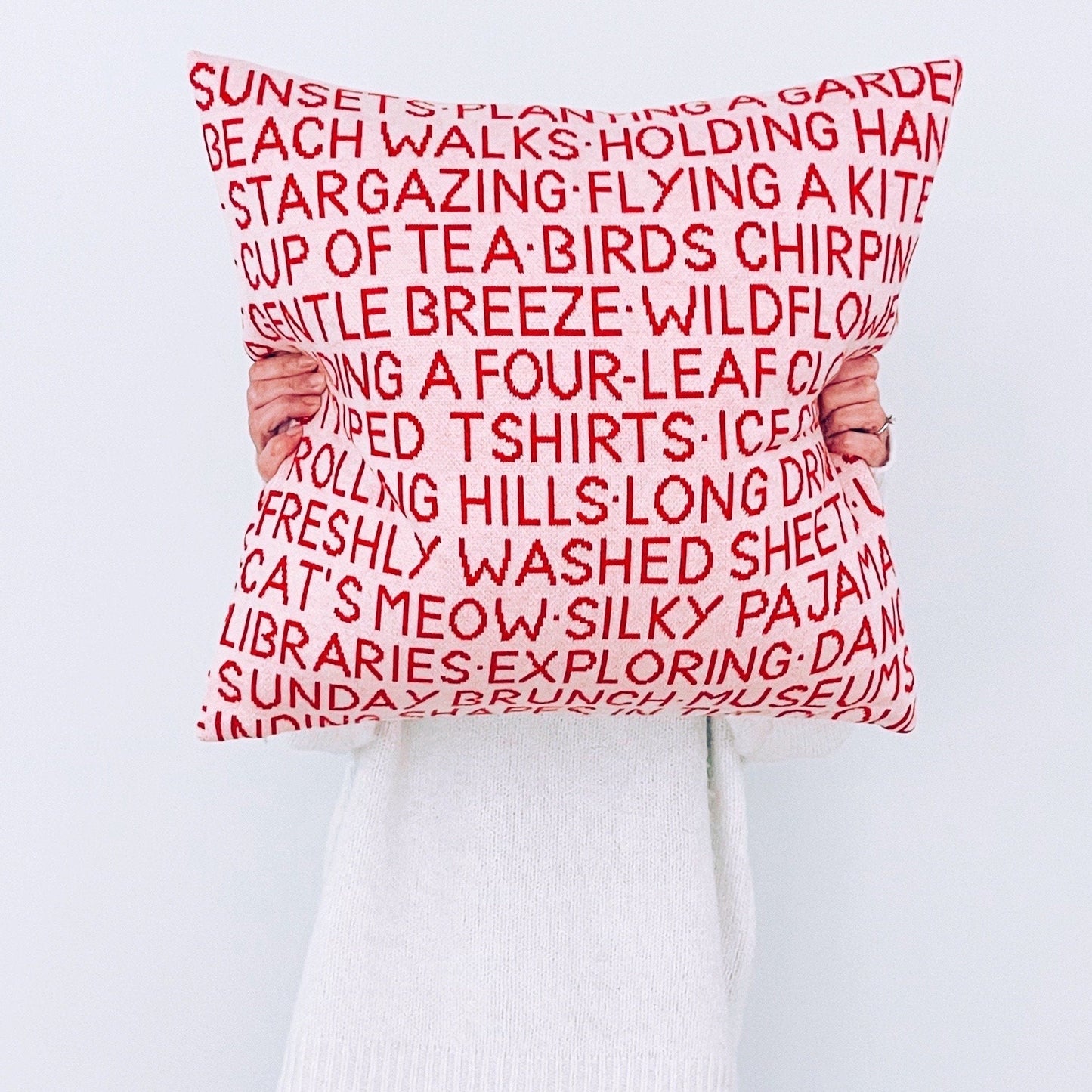 Person holding a pink pillow with red text against a white background