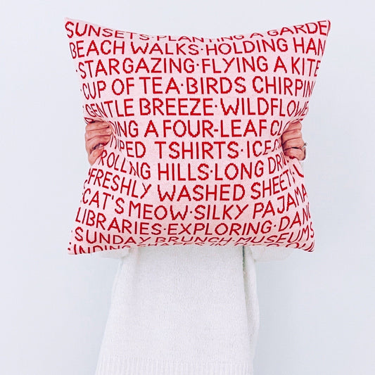 Person holding a pink pillow with red text against a white background