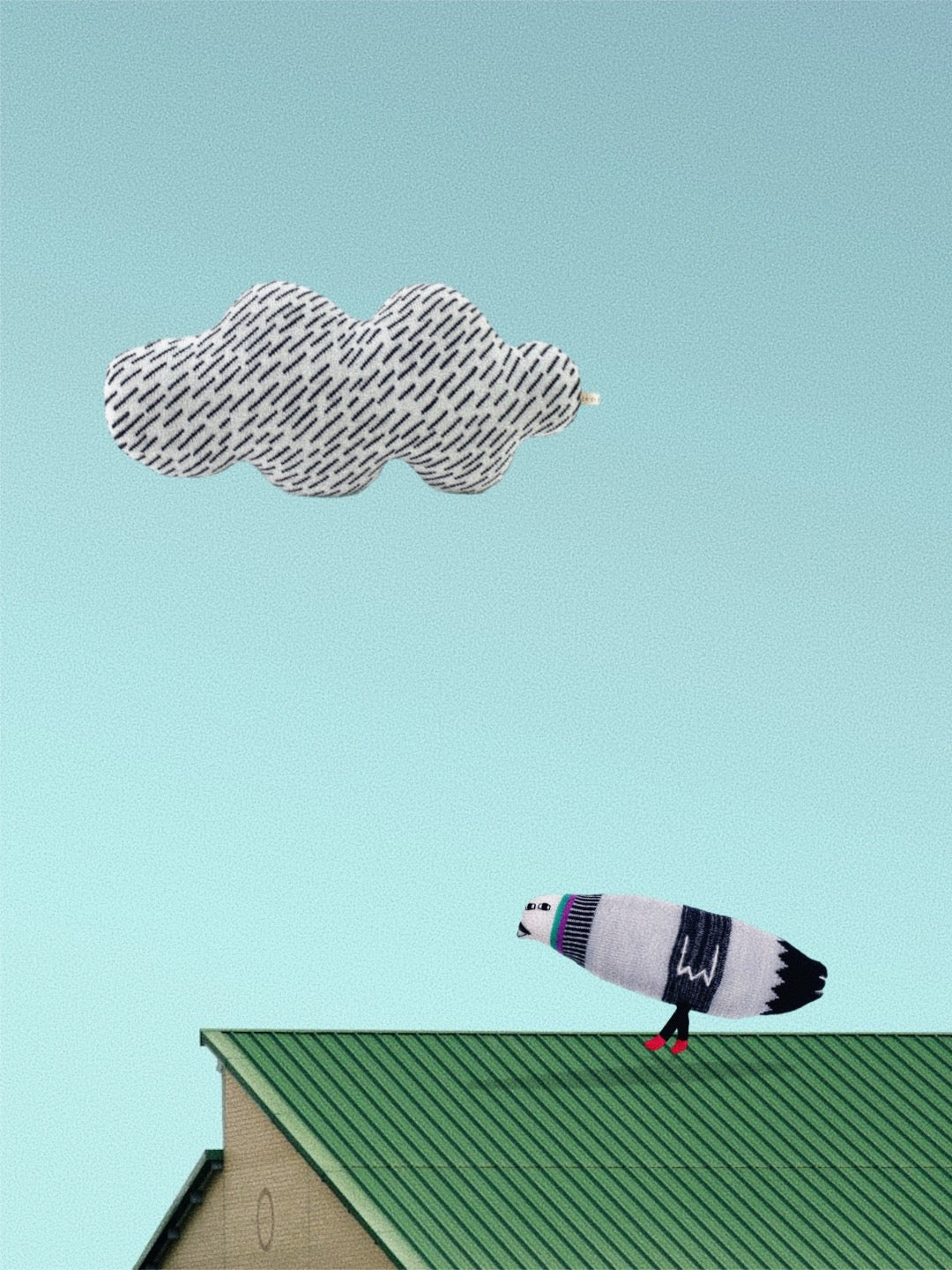Soft knitted lambswool pigeon stuffed animal plush on a green roof against a light blue sky.