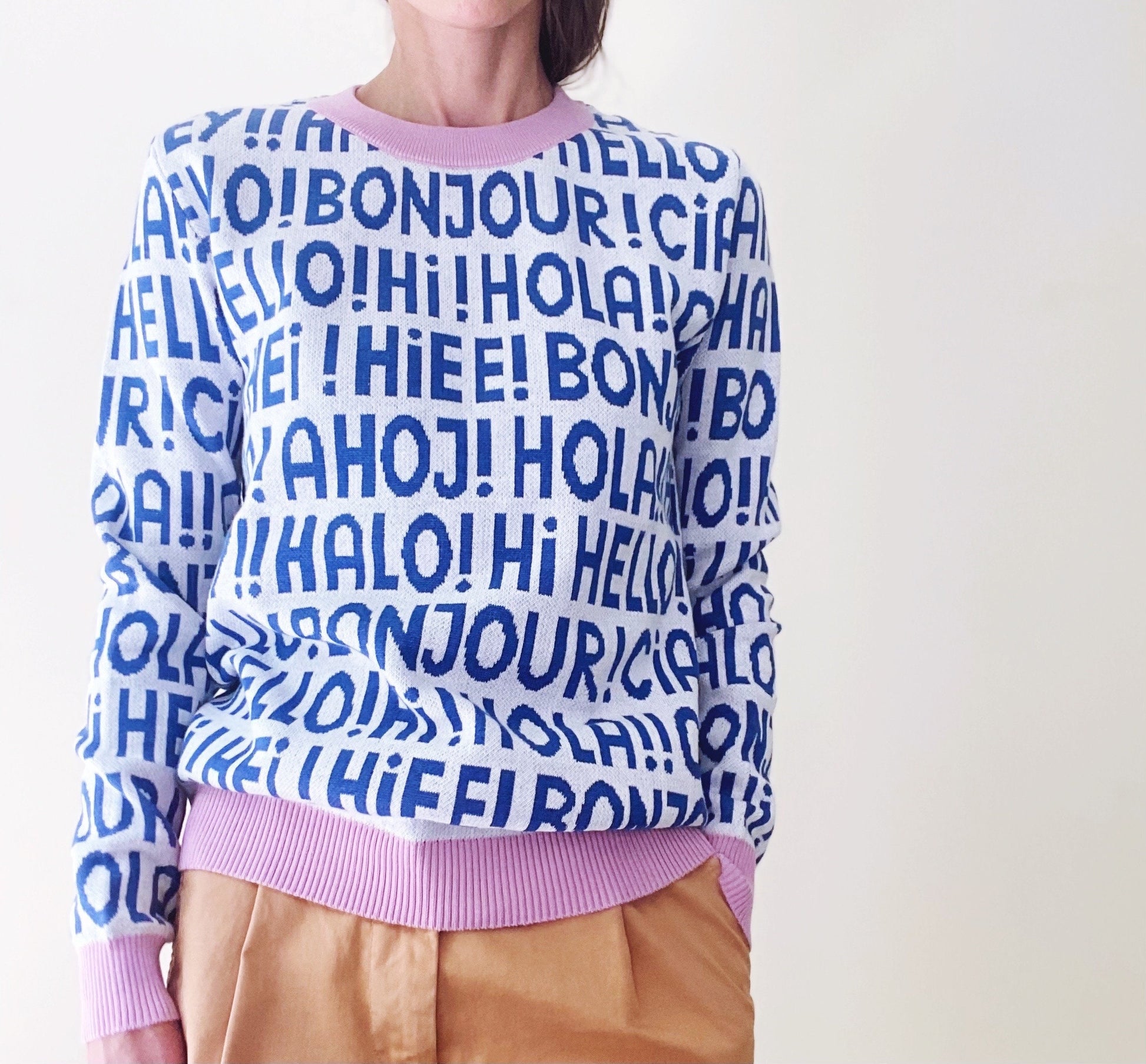 Person wearing a sweater with multilingual greetings in blue text on a white background