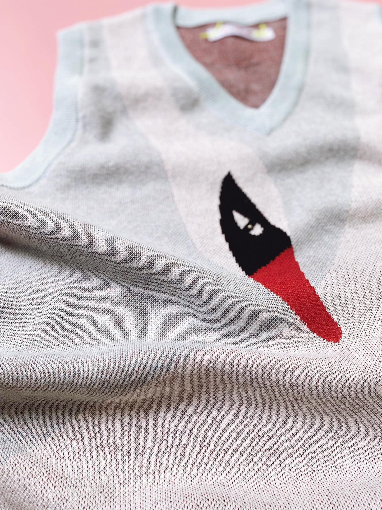 Light blue sleeveless sweater vest with a white swan graphic on a pink background
