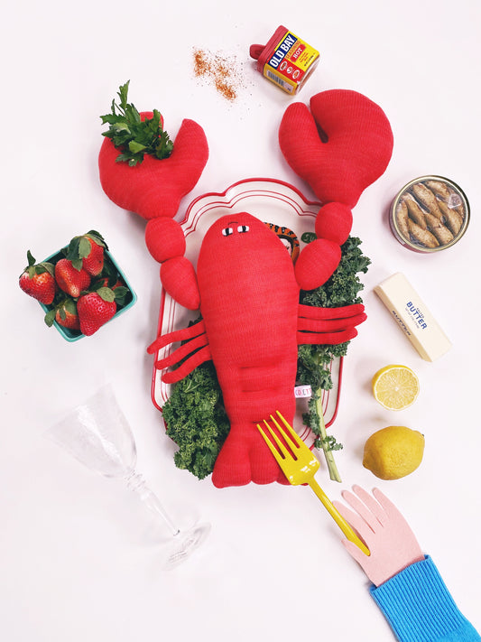 Red lobster-shaped knit plush toy cushion with vegetables on a white background