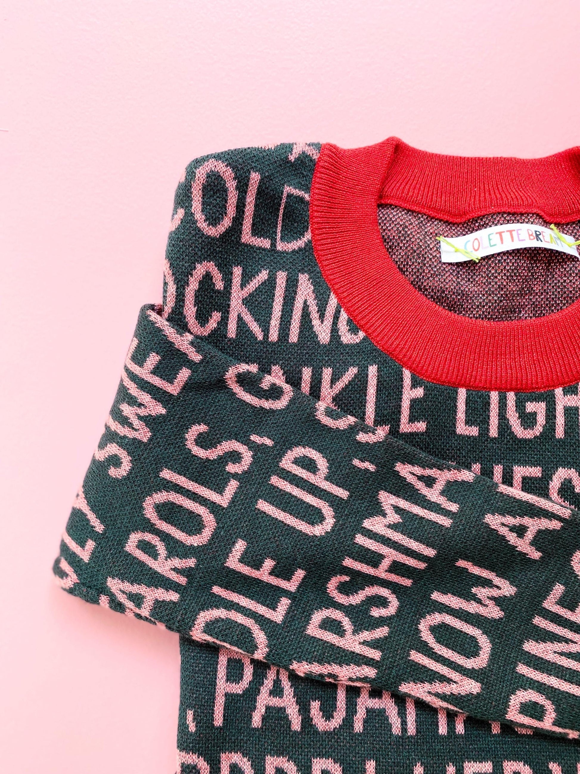 Green holiday sweater with pink festive christmas text on a pink background