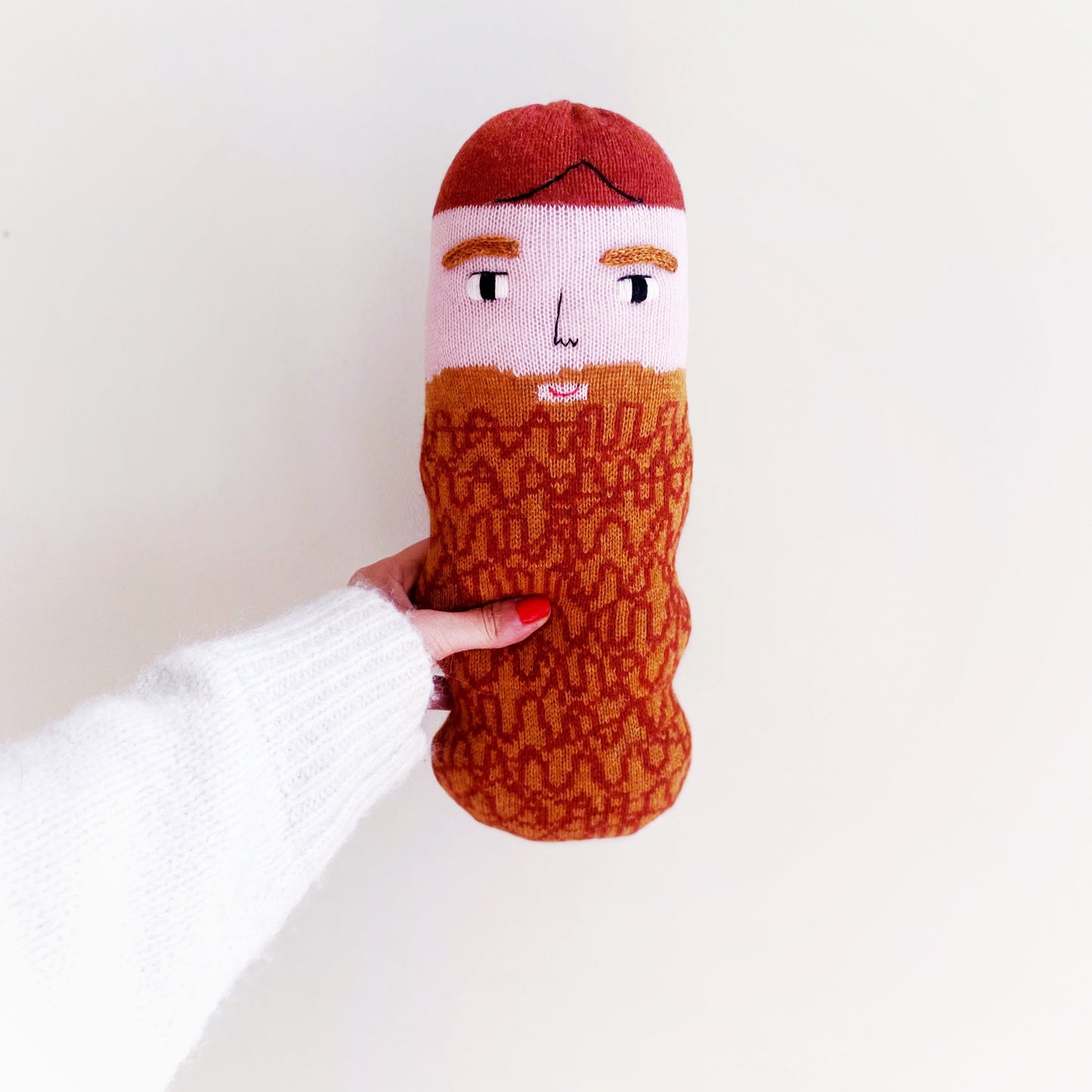Knitted lambswool plush with a face and beard design held by a person against a white background
