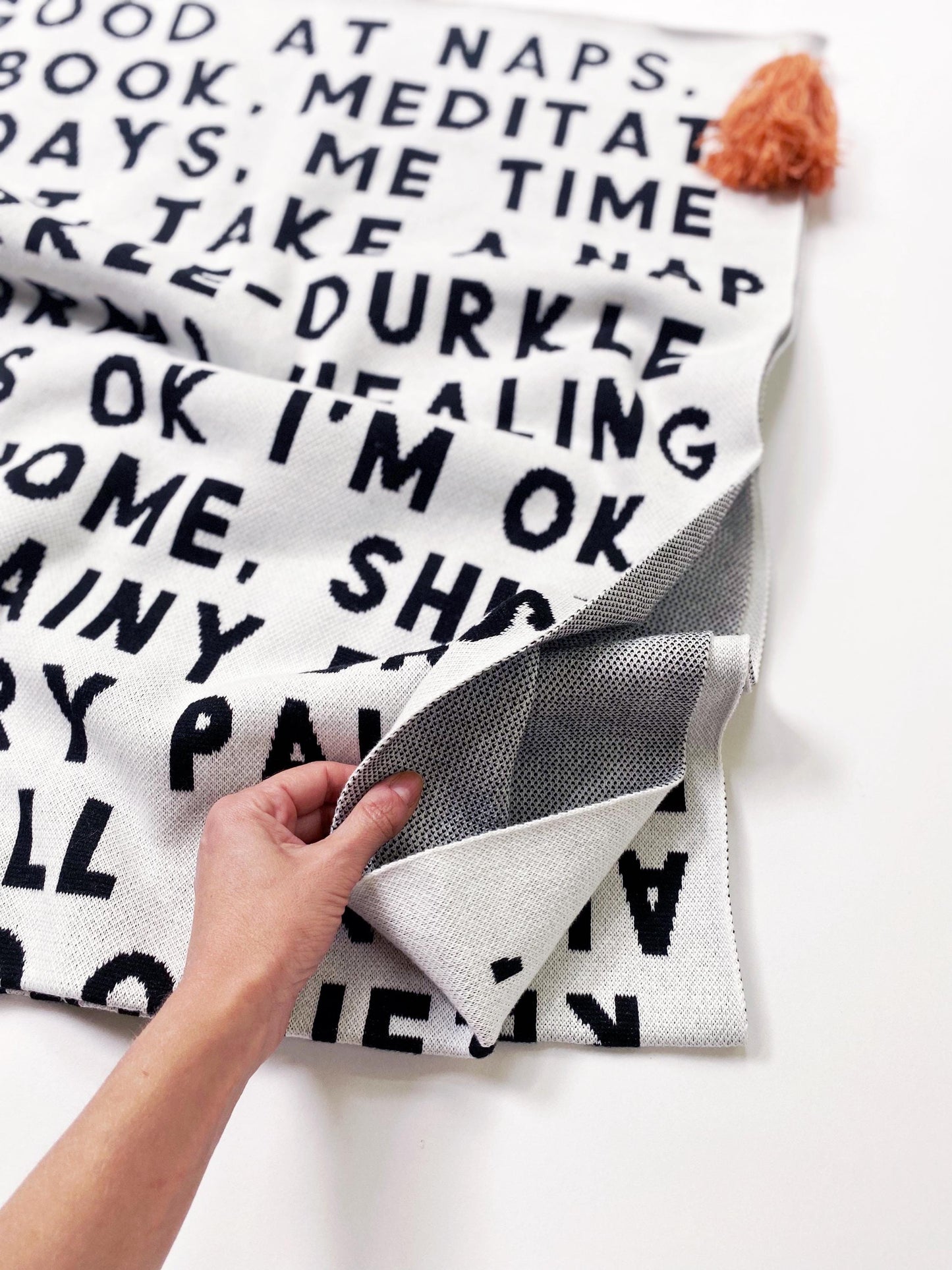 Textured blanket with black lettering held by a hand on a white background