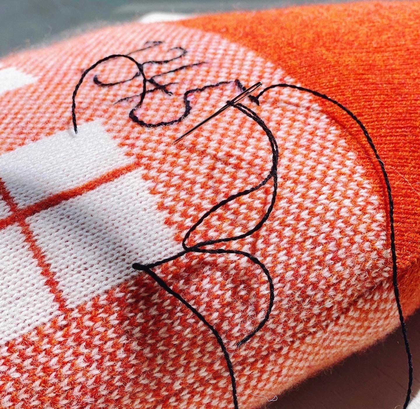 Close-up of a fabric with embroidered design on an orange and white checkered background.
