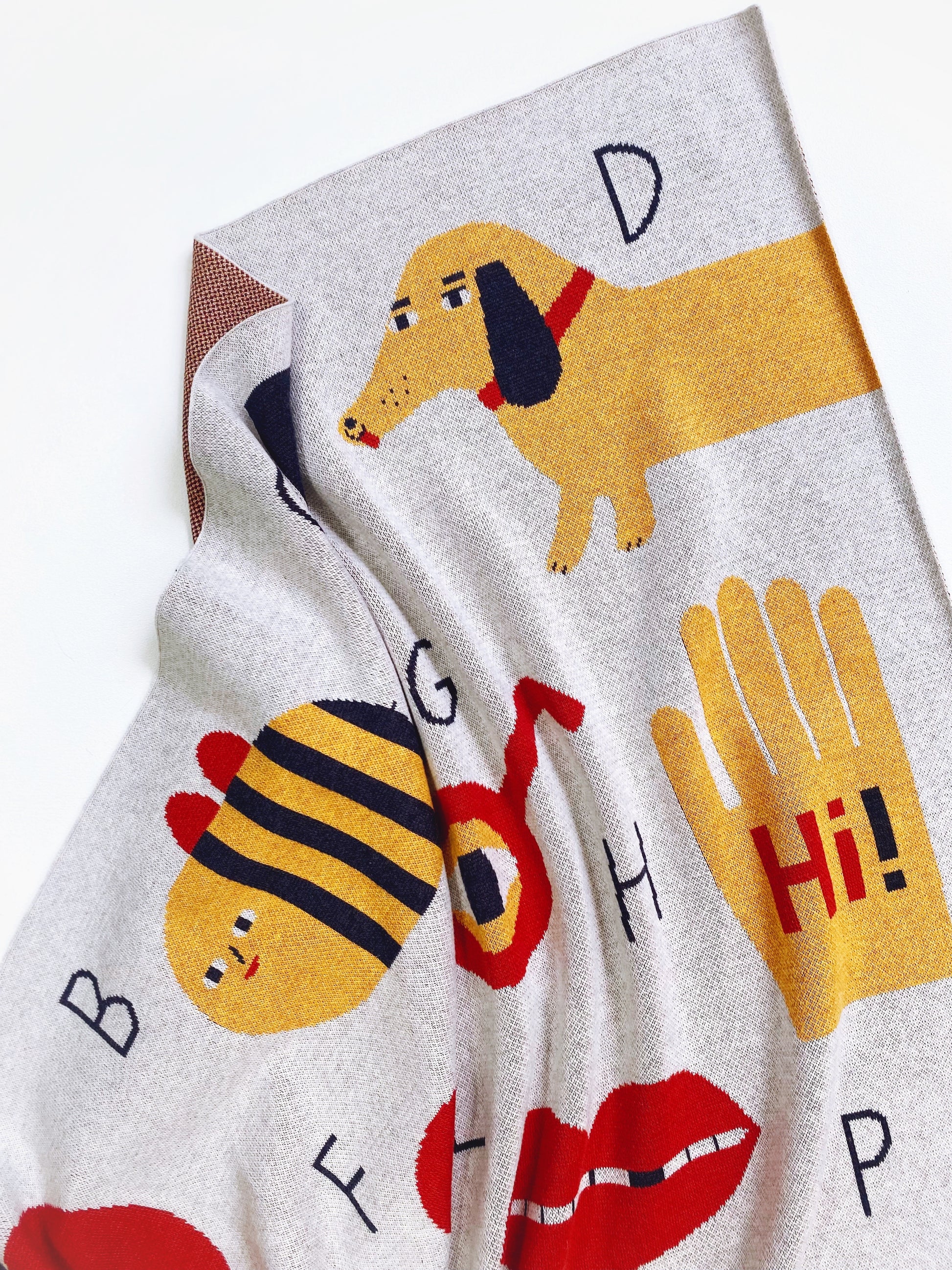 Alphabet knit blanket with cartoon dog, bee, and letters on a white background