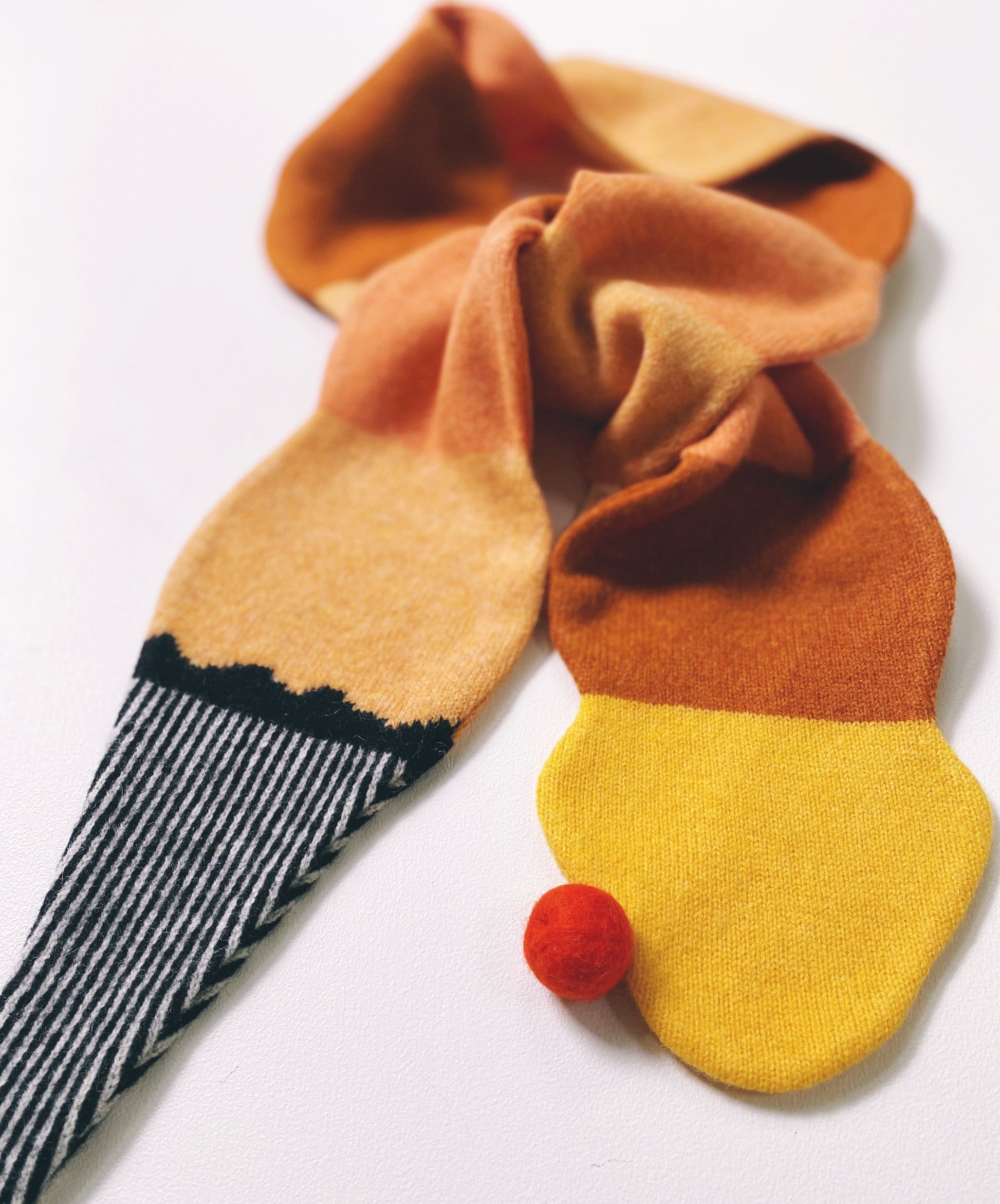 Colorful knitted lambswool scarf shaped like an ice cream with a red pom-pom on a white background