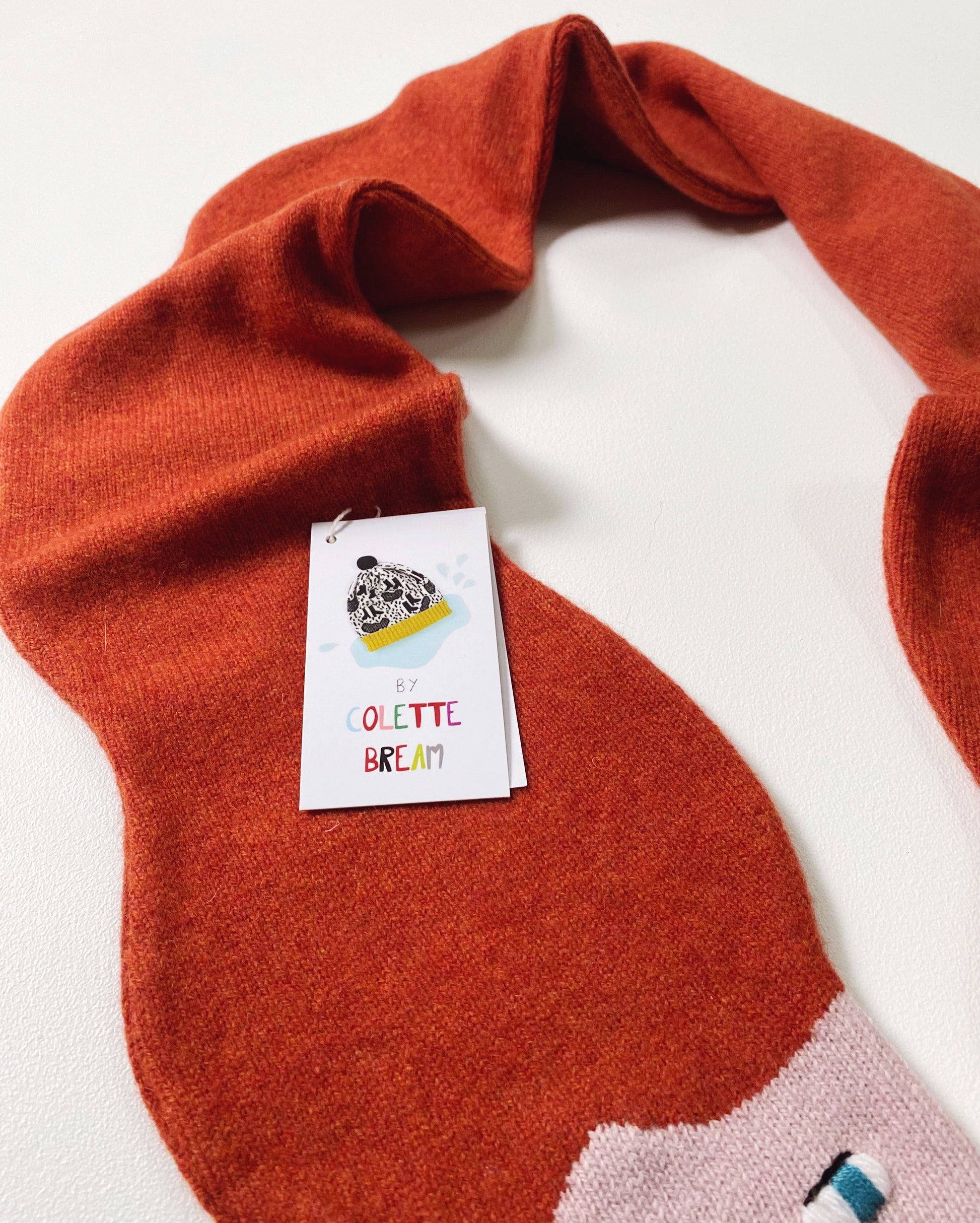 Orange red knitted lambswool scarf with a brand tag on a white background