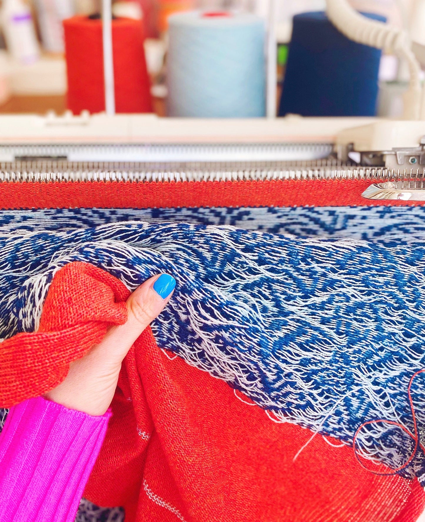 Textile with red and blue pattern, held by a person wearing a pink sleeve.