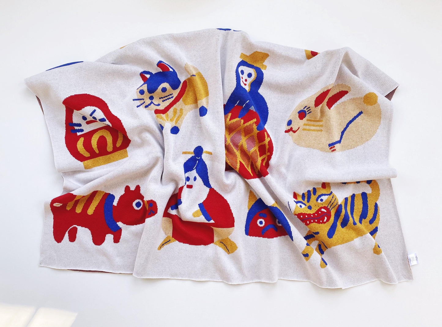 Folded knit blanket with colorful cartoon animal designs and other japanese characters and folk toys on a white background