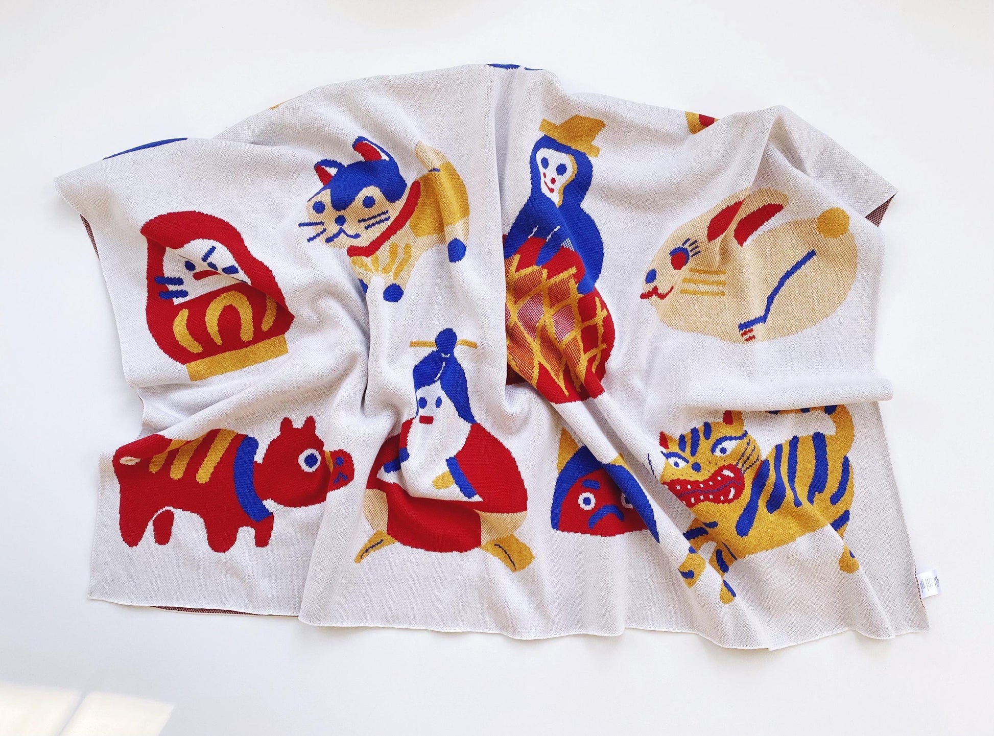 Folded knit blanket with colorful cartoon animal designs and other japanese characters and folk toys on a white background