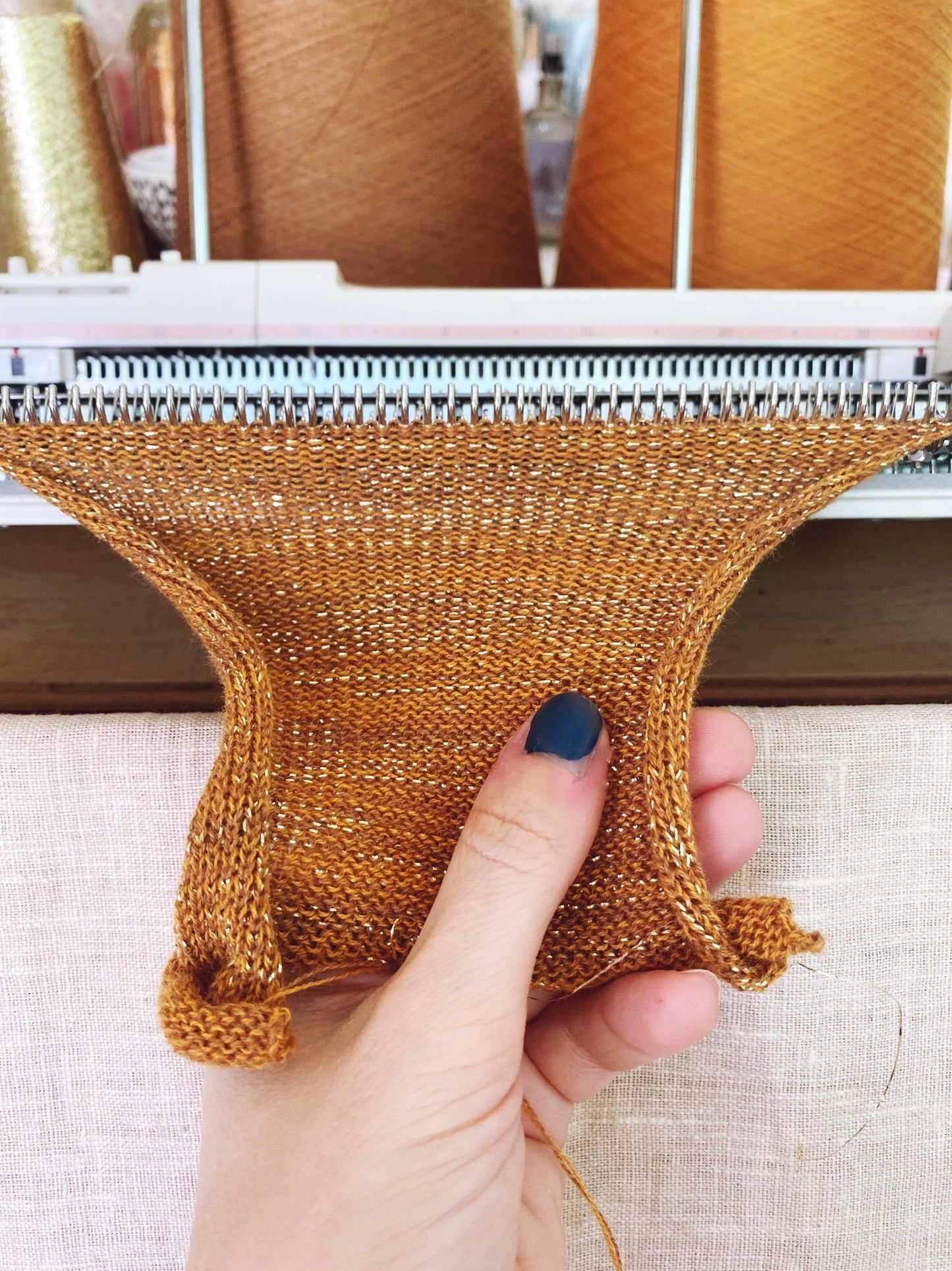 Hand holding a knitted brown fabric sample with knitting machine in the background