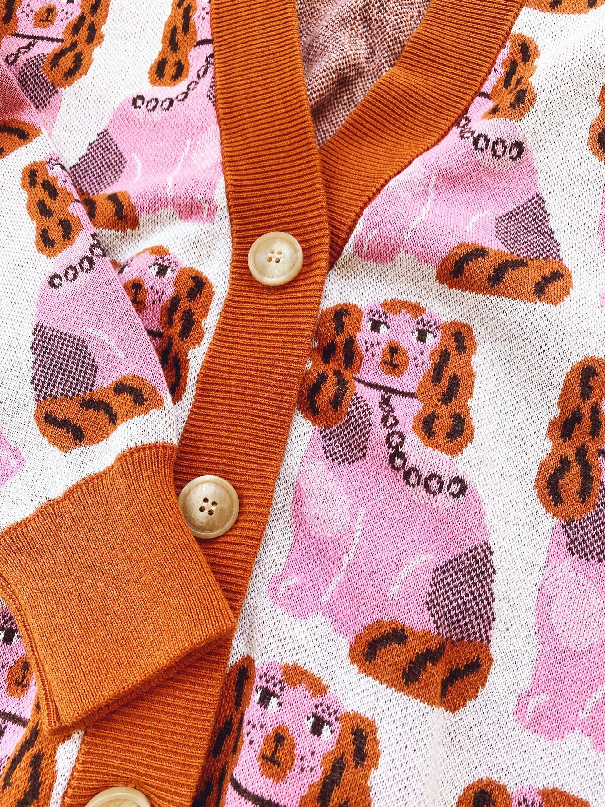 Close-up of a knitted cardigan sweater with a pink pattern featuring cartoon of staffordshire dogs and buttons.