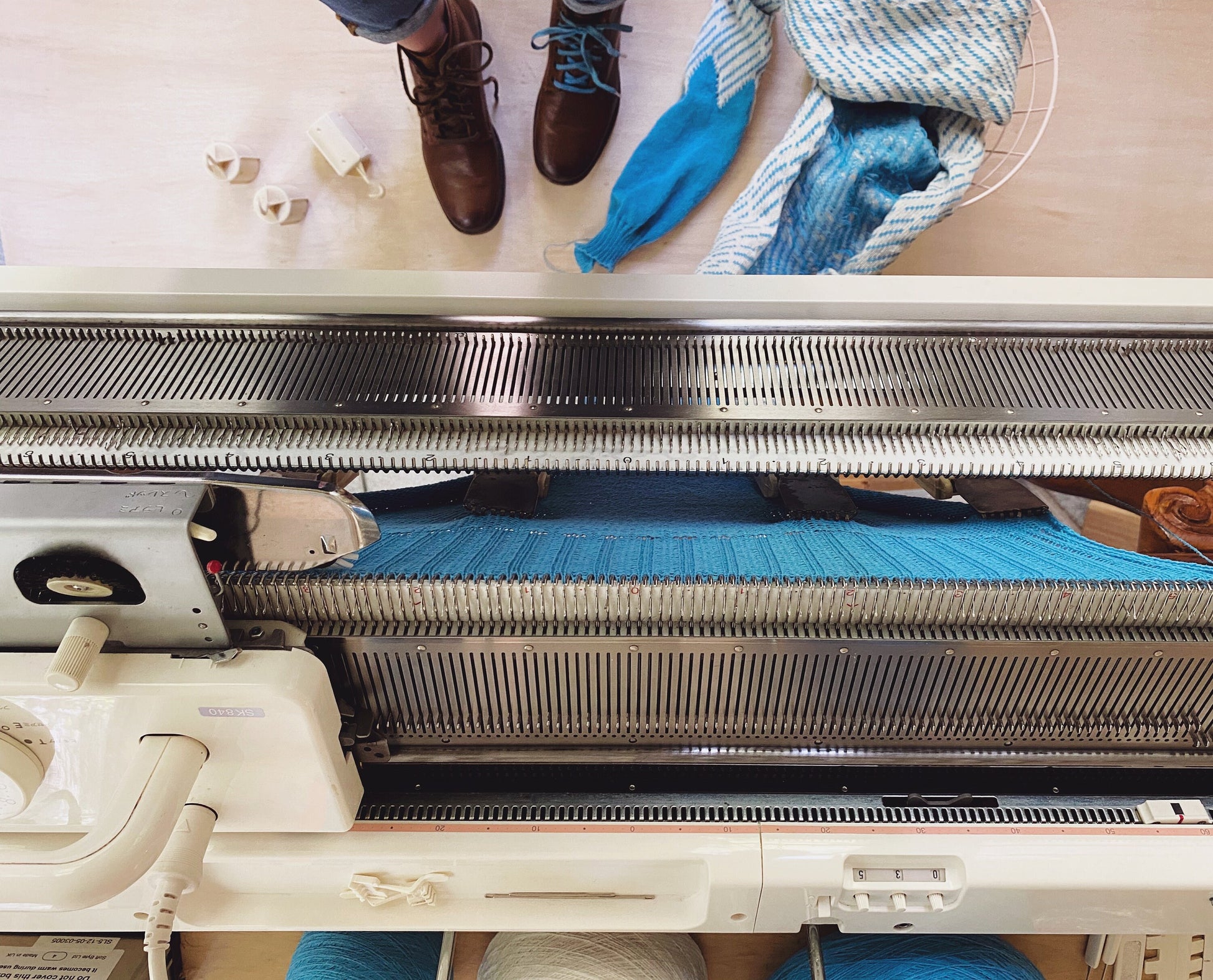 Knitting machine with blue yarn and a partially completed sweater on a wooden surface.