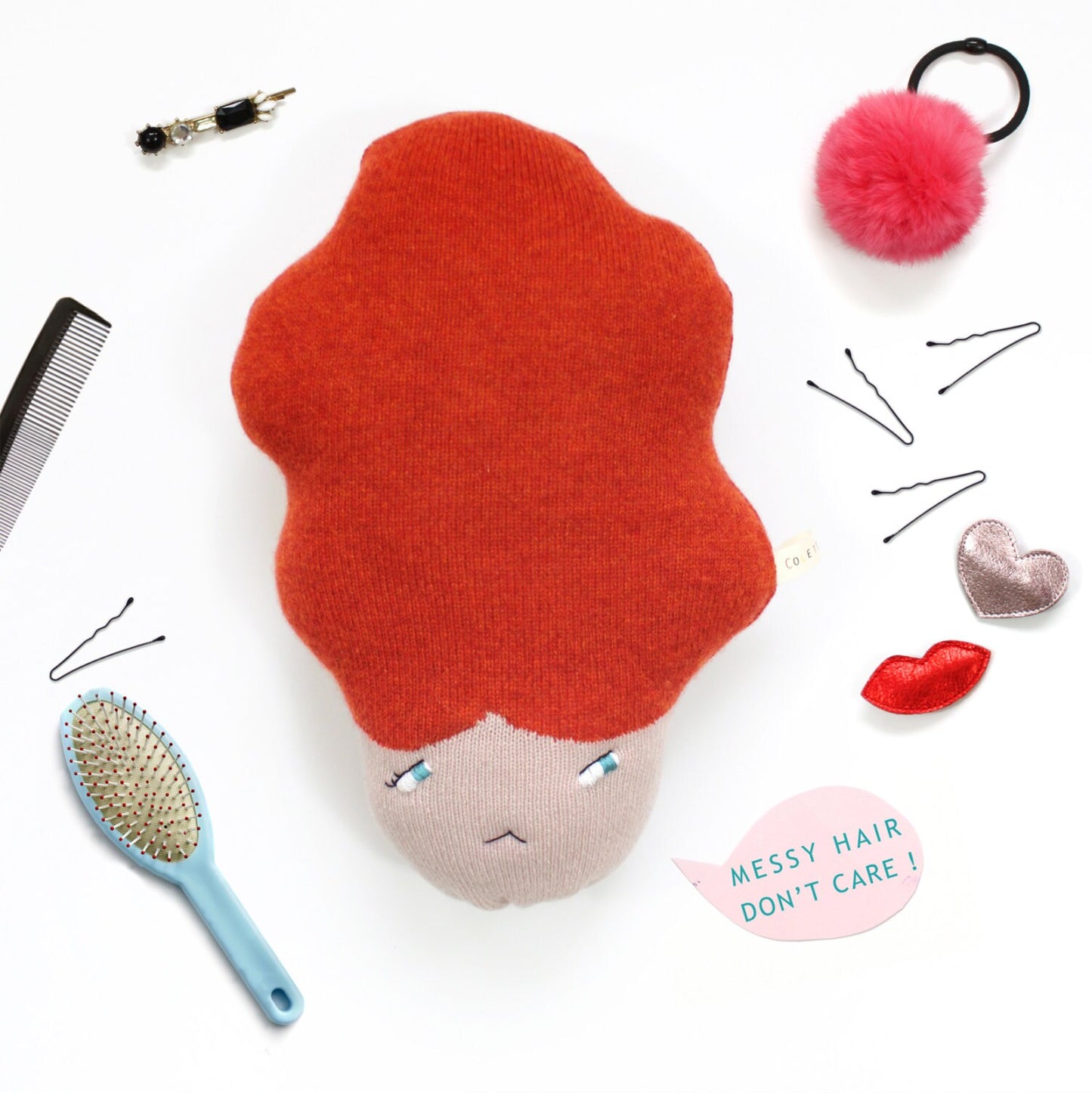 Plush toy with red hair, comb, brush, and hair accessories on a white background