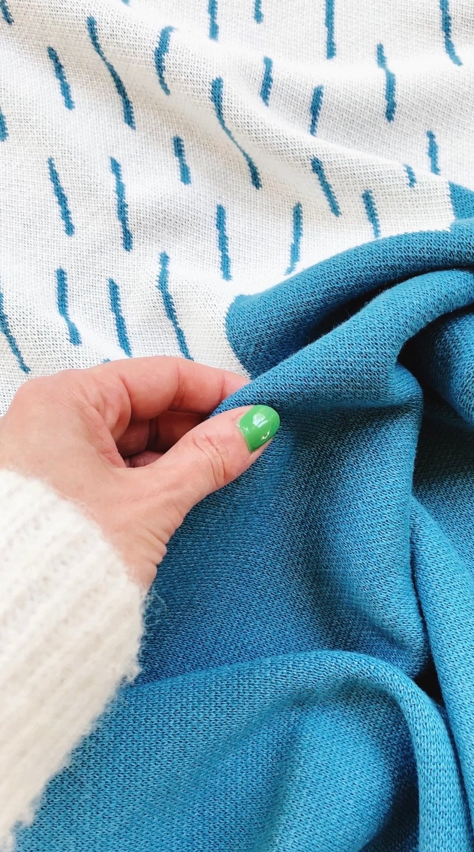 Hand holding blue knit fabric with white background featuring blue lines