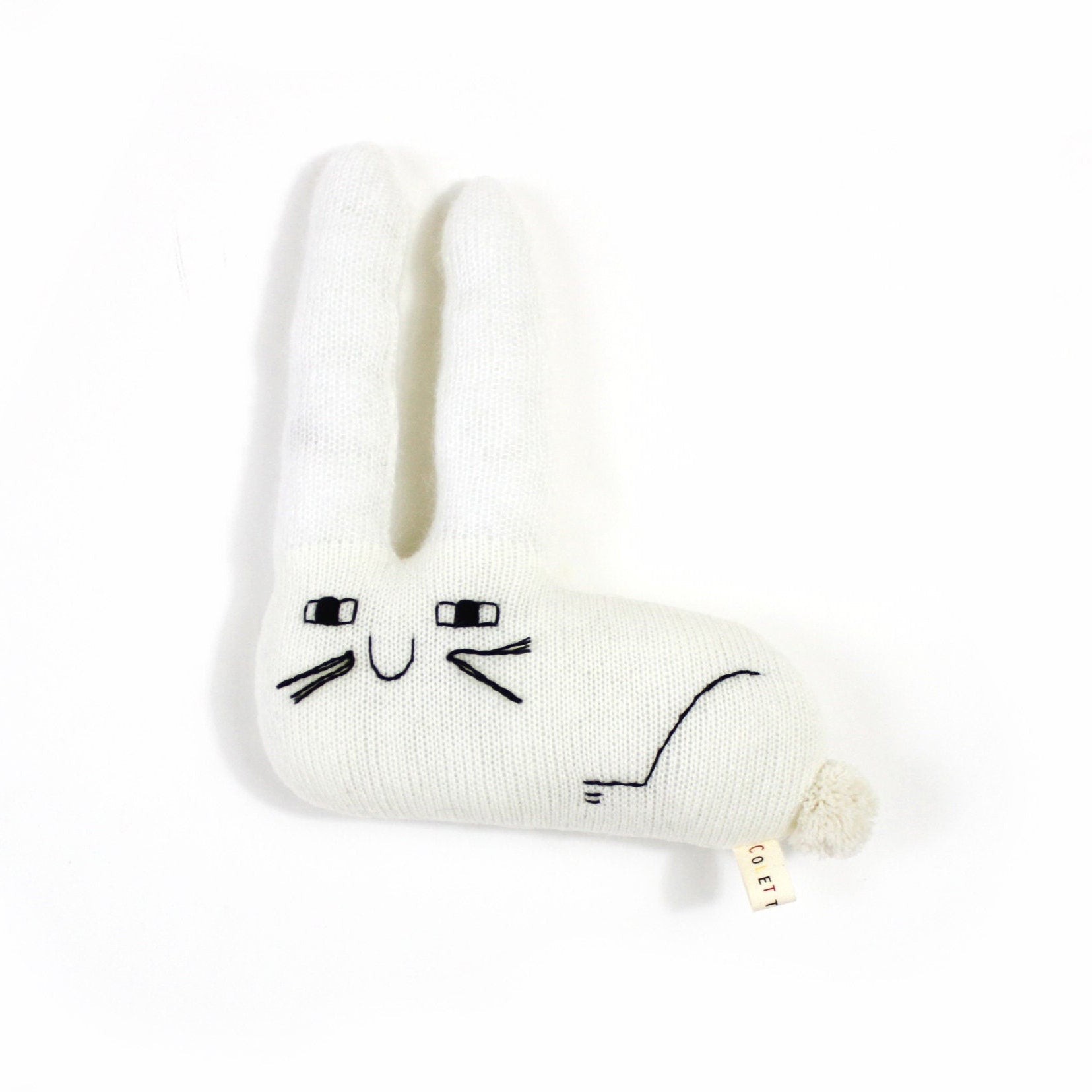 White knitted bunny shaped plush toy with happy face design on a white background